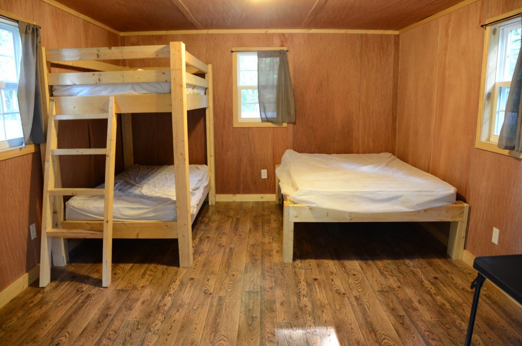 Interior view of a camping cabin showing two bunk beds and one double be.
